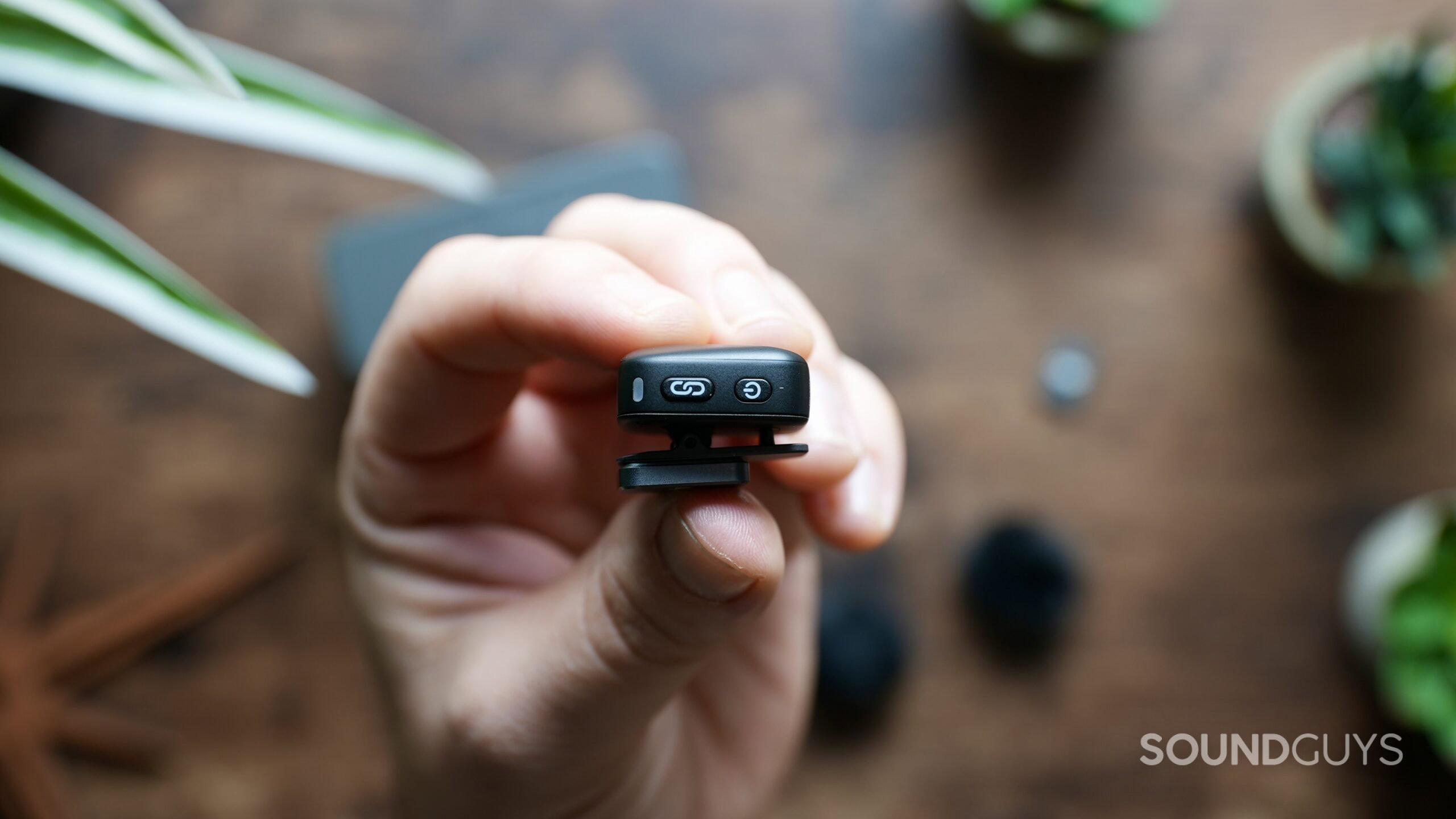 A hand holds a DJI Mic Mini transmitter, showing it's link and power buttons.