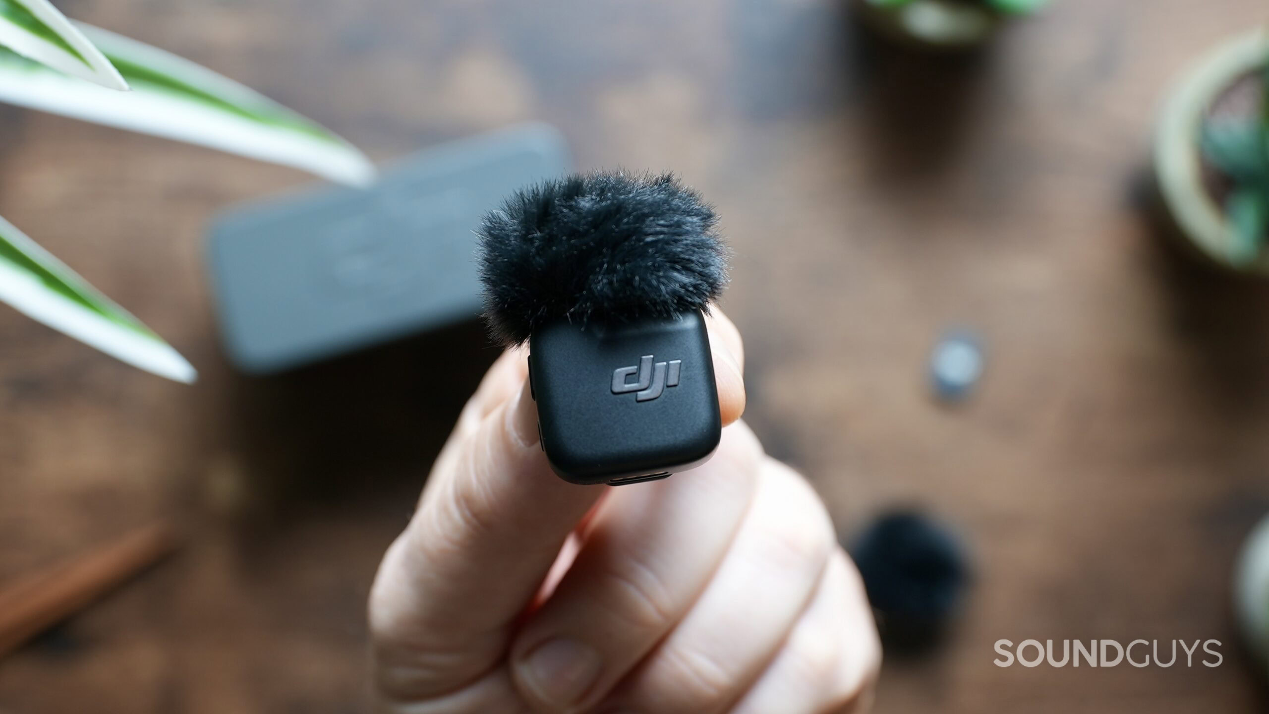 A hand holds a DJI Mic Mini transmitter with its windscreen attached.