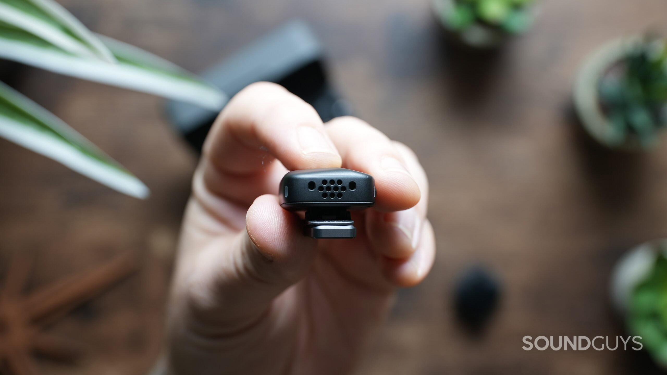 A hand holds a DJI Mic Mini transmitter, showing it's microphone.