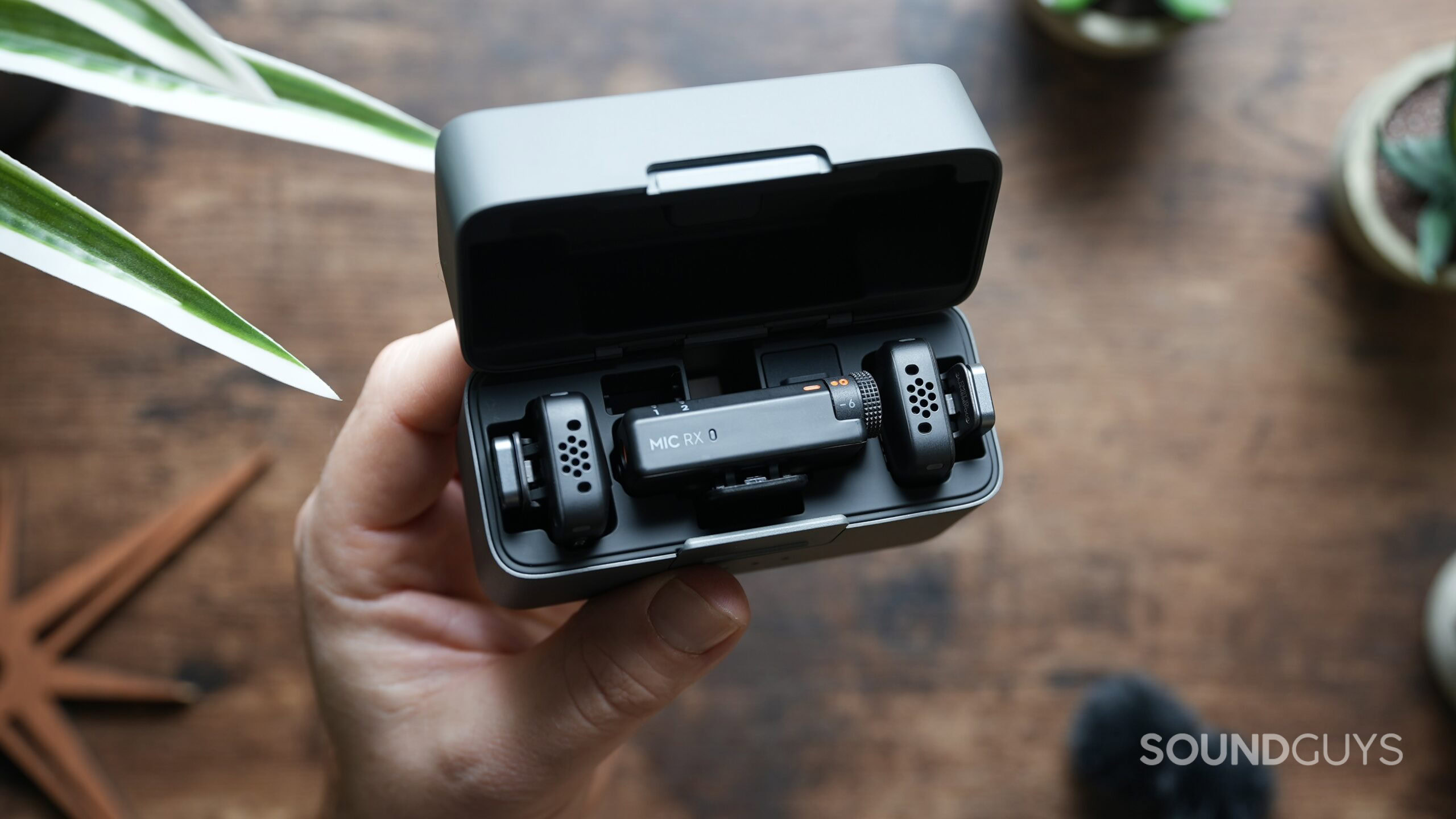 A hand holds the DJI Mic Mini charging case with the lid open, showing the transmitters and receivers.