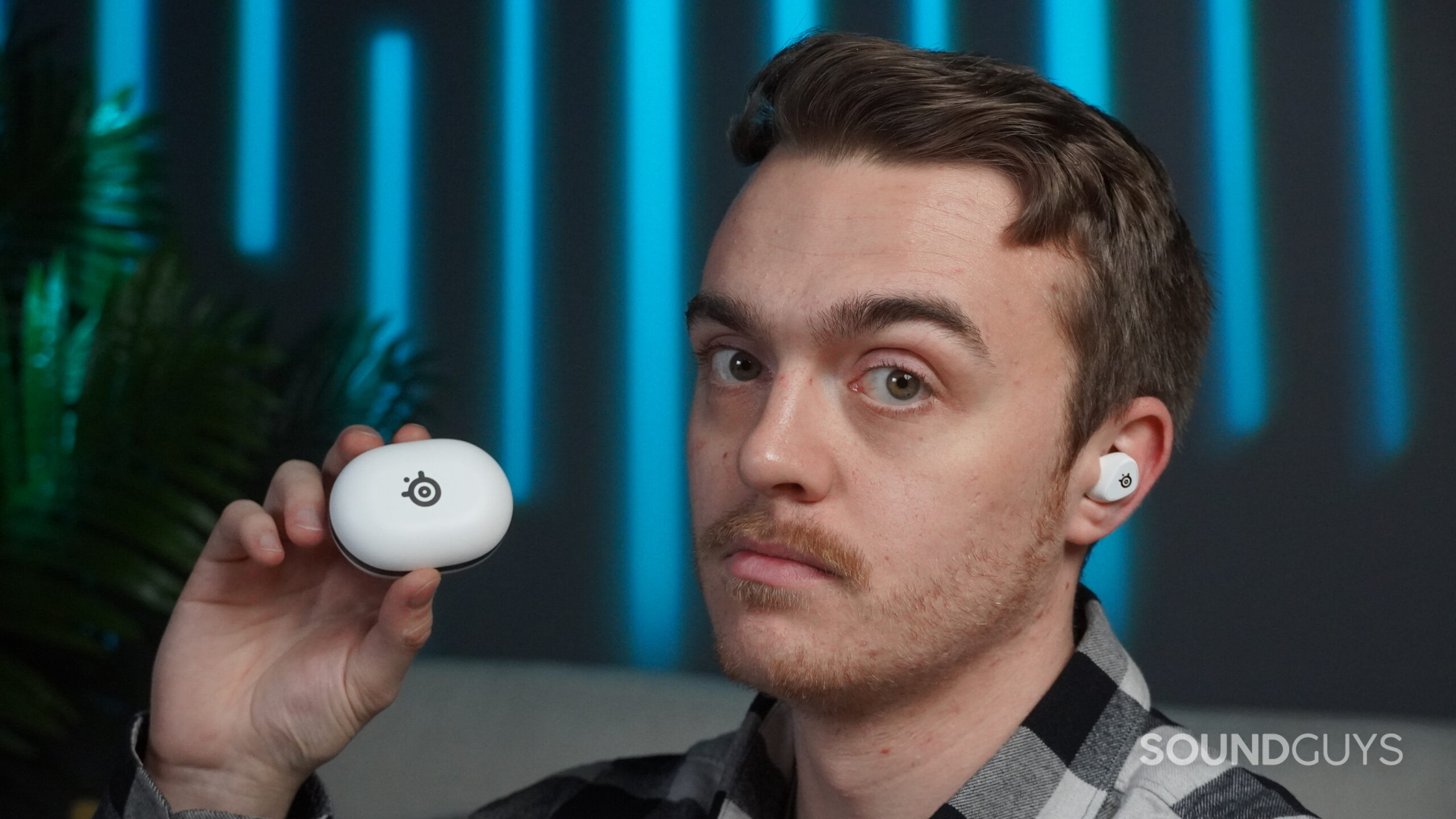 A handsome young man holding the steelseries gamebuds