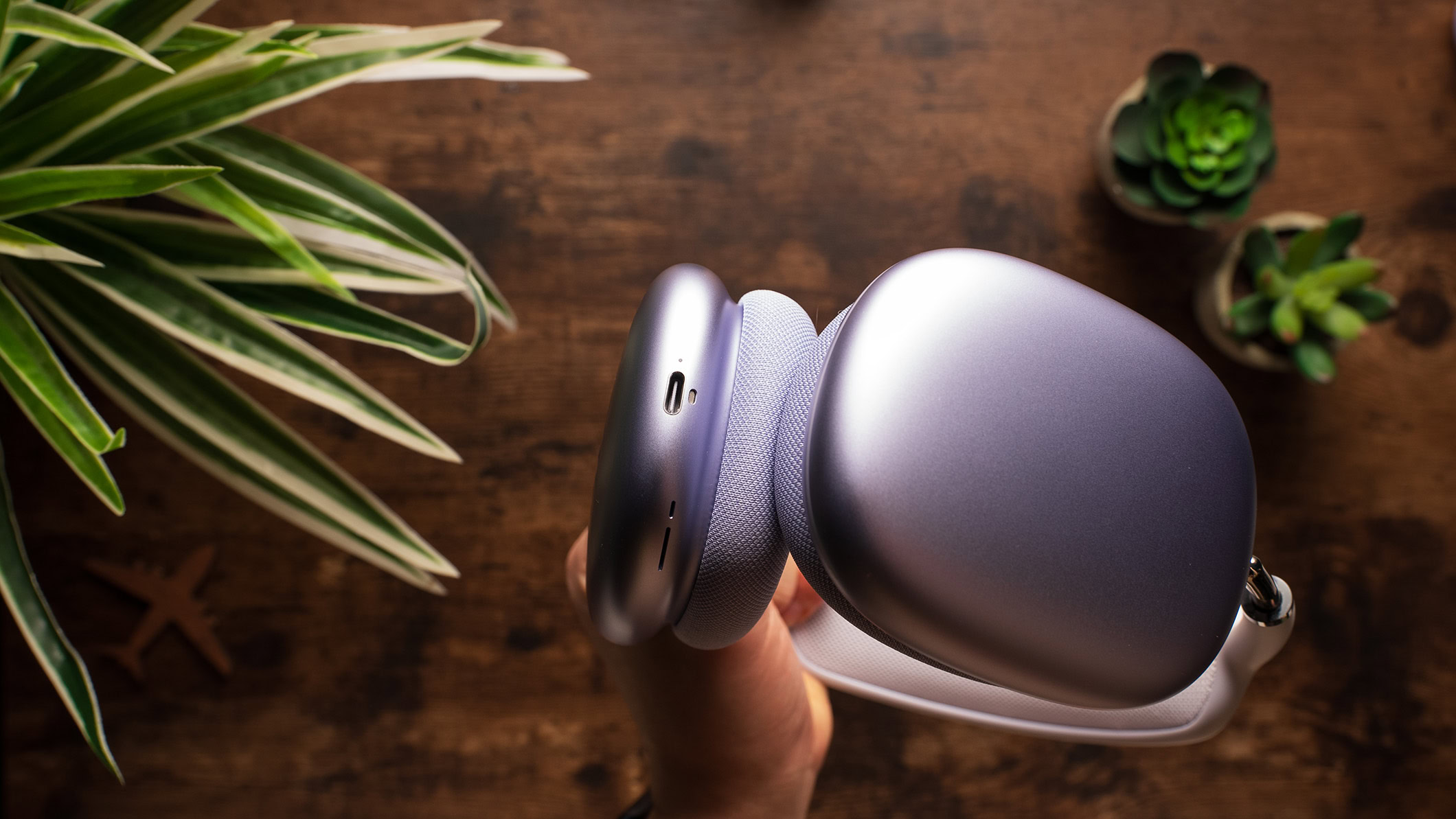 A hand holds the AirPods Max showing the USB-C charging port.