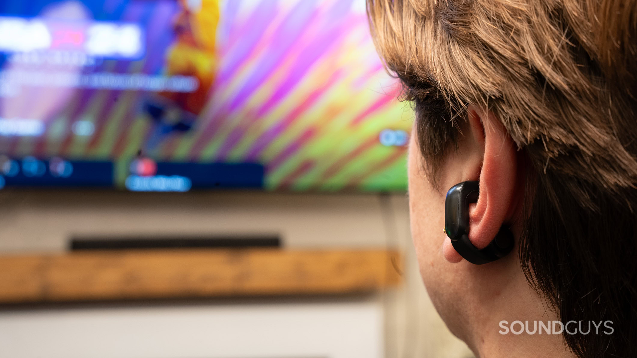 A man wearing the Bose Ultra Open Earbuds looking at a TV with the Bose Smart Soundbar. 