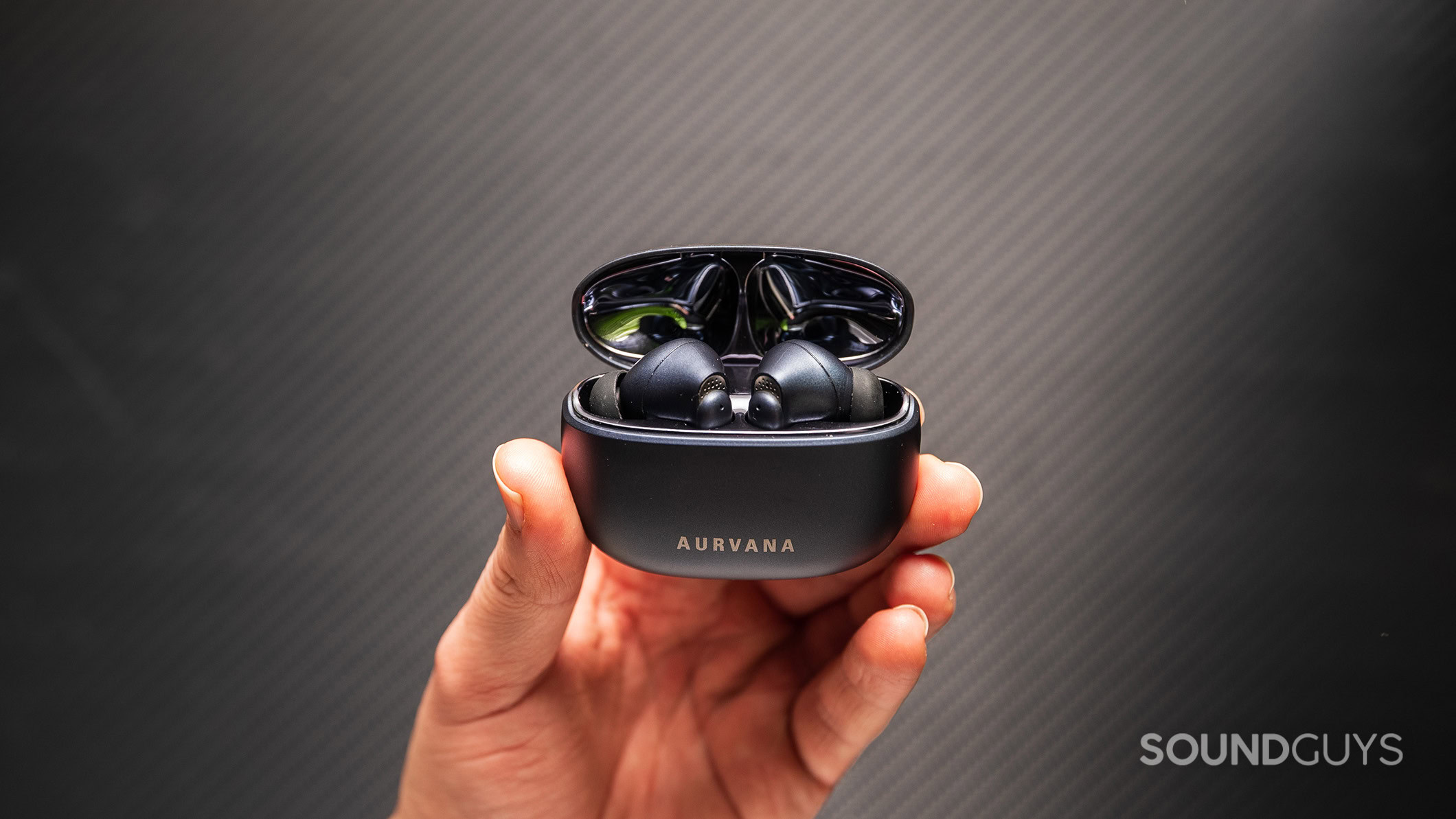 A hand holding the Creative Aurvana Ace Mimi earbuds in their charging case.