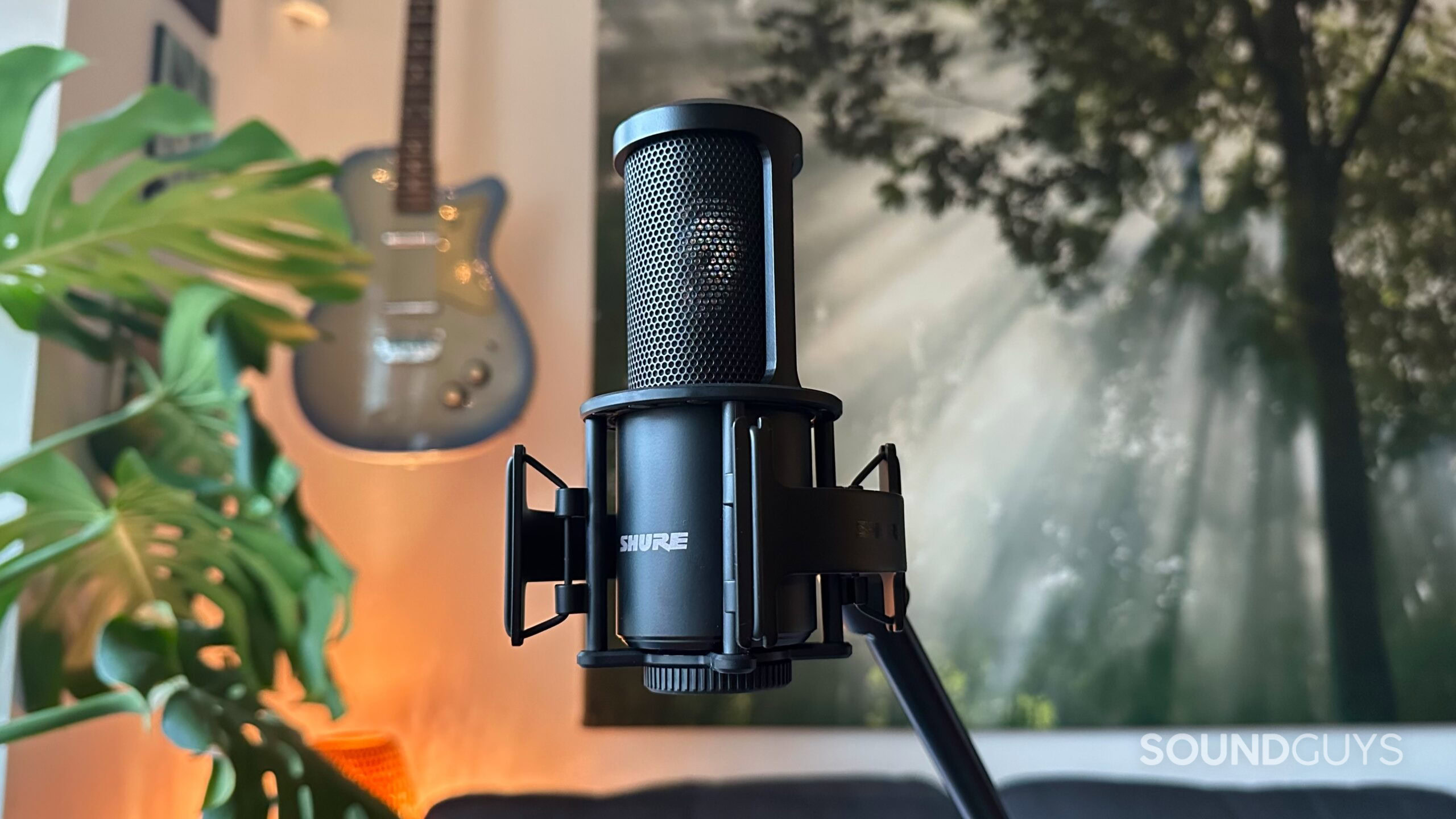 A Shure SM4 microphone mounted on a mic stand with a guitar in the background.