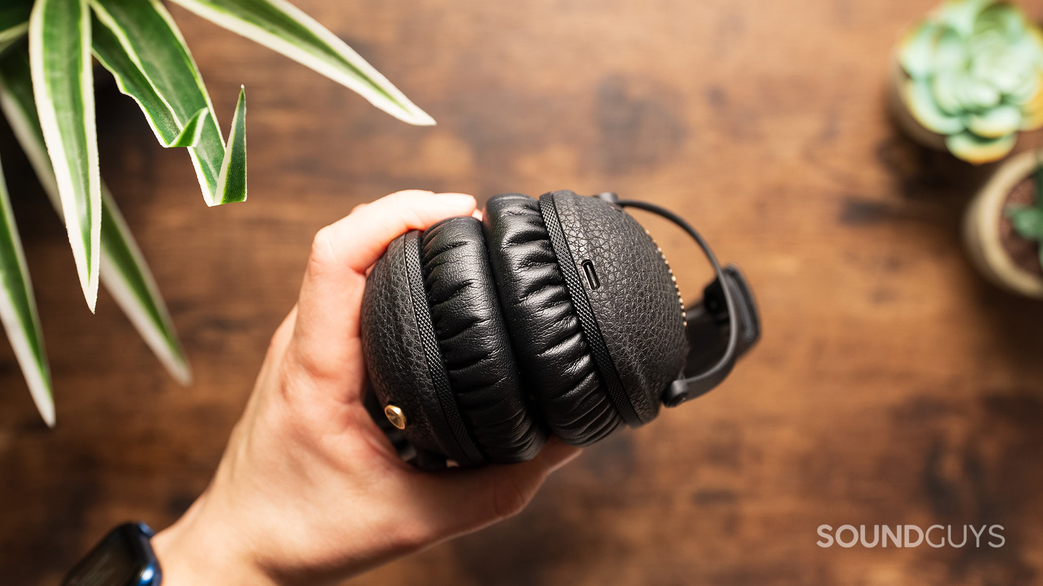 A hand holds the Marshall Monitor III ANC headphones showing the USB-C port. 