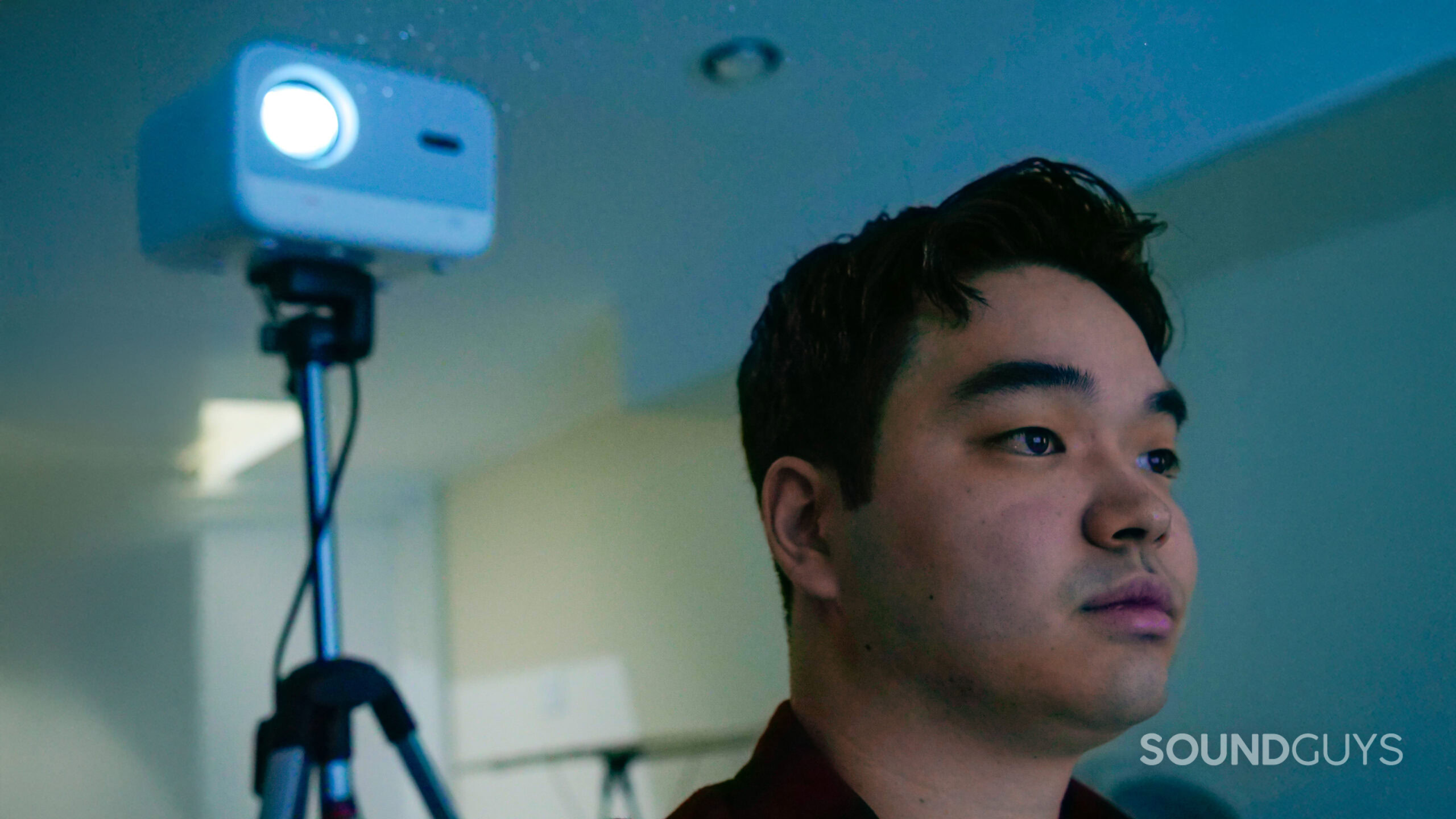 A man watching a movie projected by a Yaber L2s Projector on a stand in a dark home theater room