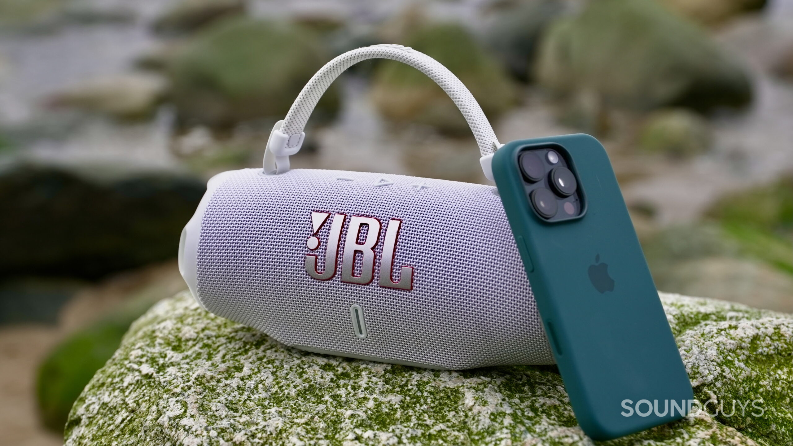 An iPhone 16 Pro resting against a JBL Charge 6.