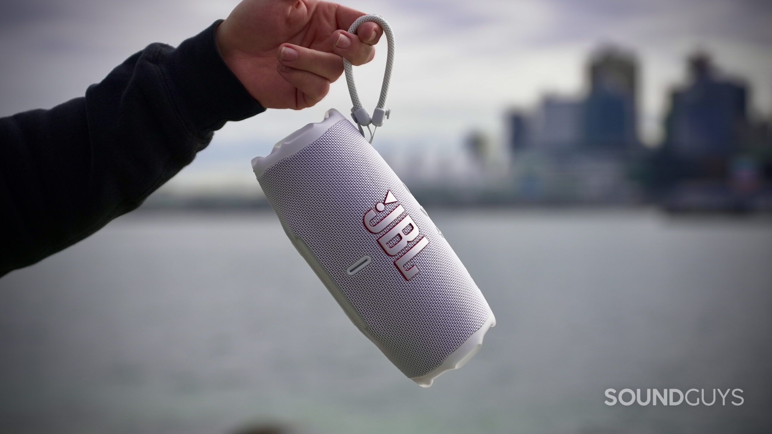 A hand holds the JBL Flip Charge 6 speaker by it's attachment strap.