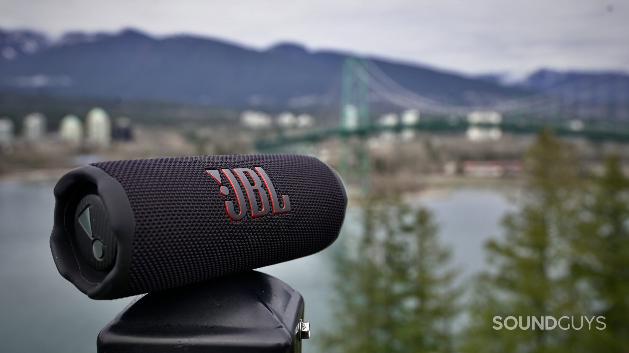 A JBL Flip 7 resting on a railing with nature in the back ground.