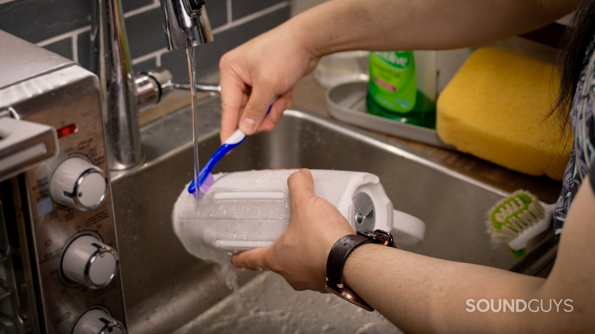 Cleaning the JBL Charge 6 with a brush underneath running tap